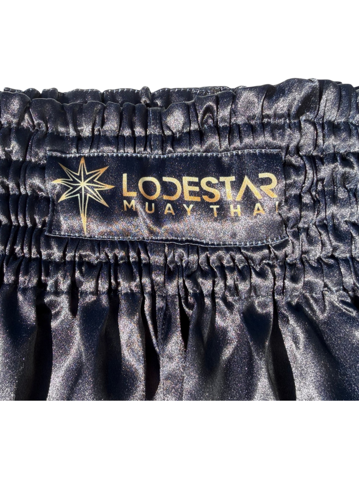 Lodestar Muay Thai black polyester shorts with elastic waistband and side openings for enhanced range of motion.