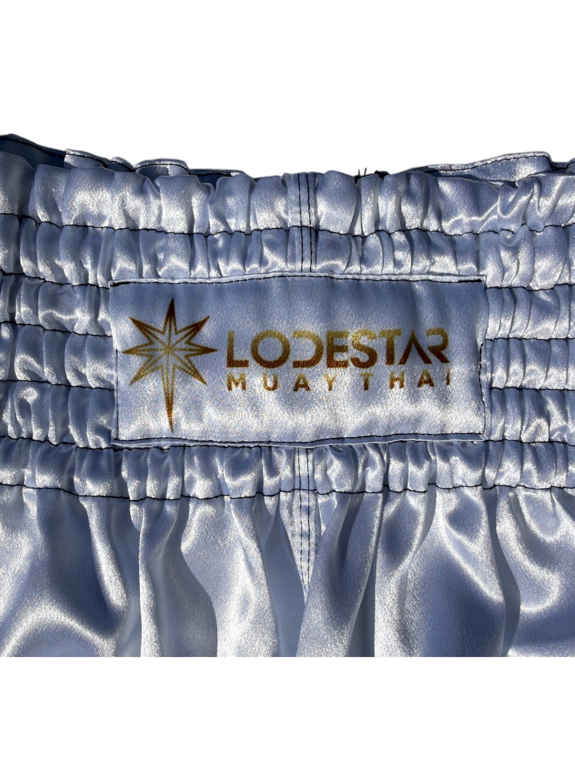Lodestar Muay Thai shorts in light blue satin with elastic waistband and side openings for enhanced range of motion.